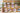Drewniana fototablica ze zawieszonymi Zdjęciami Retro przymocowanymi do sznurków klamerkami do bielizny przedstawiająca gości weselnych. Całość stoi przed kamienną ścianą na trawniku.